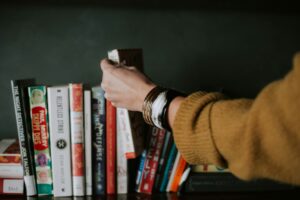A selection of books on a shelf with someone's arm and hand selecting a book