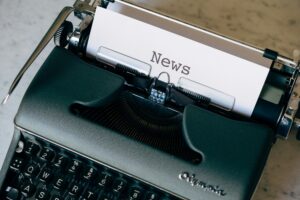 Picture Description: A manual typewriter, seen from above, with a piece of paper in it, with the word 'news' typed in capitals at the top.